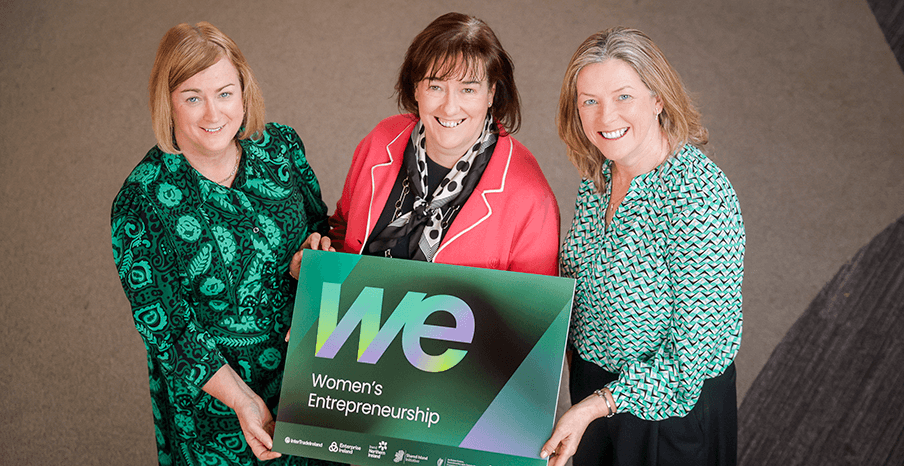 Three women are holding a sign to promote new programmes for women's entrepreneurship