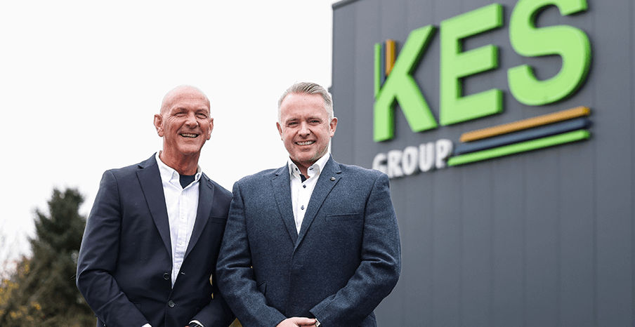 Two men standing in front of KES Group sign on factory