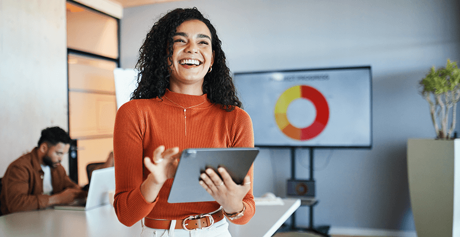 A woman is standing in an office, holding a tablet and smiling 