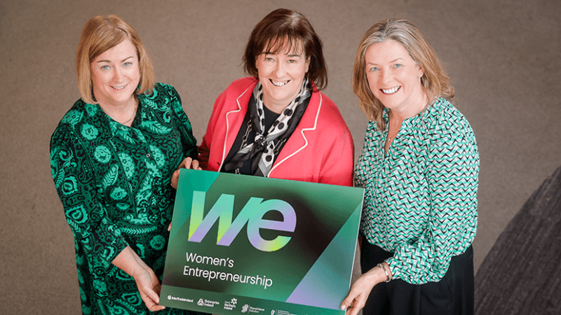 Three women are holding a sign to promote new programmes for women's entrepreneurship