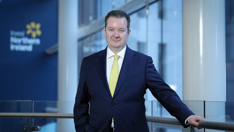 Kieran Donoghue, Invest NI CEO, is standing on a balcony in front of the Invest NI logo